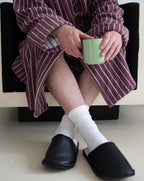 Person wearing a striped robe, white socks, and black slippers holding a green mug.