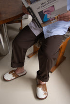 Person wearing brown shoes with white soles, sitting on a chair holding a book.