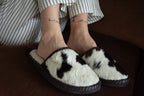Person wearing white slippers with black patterns on a brown surface