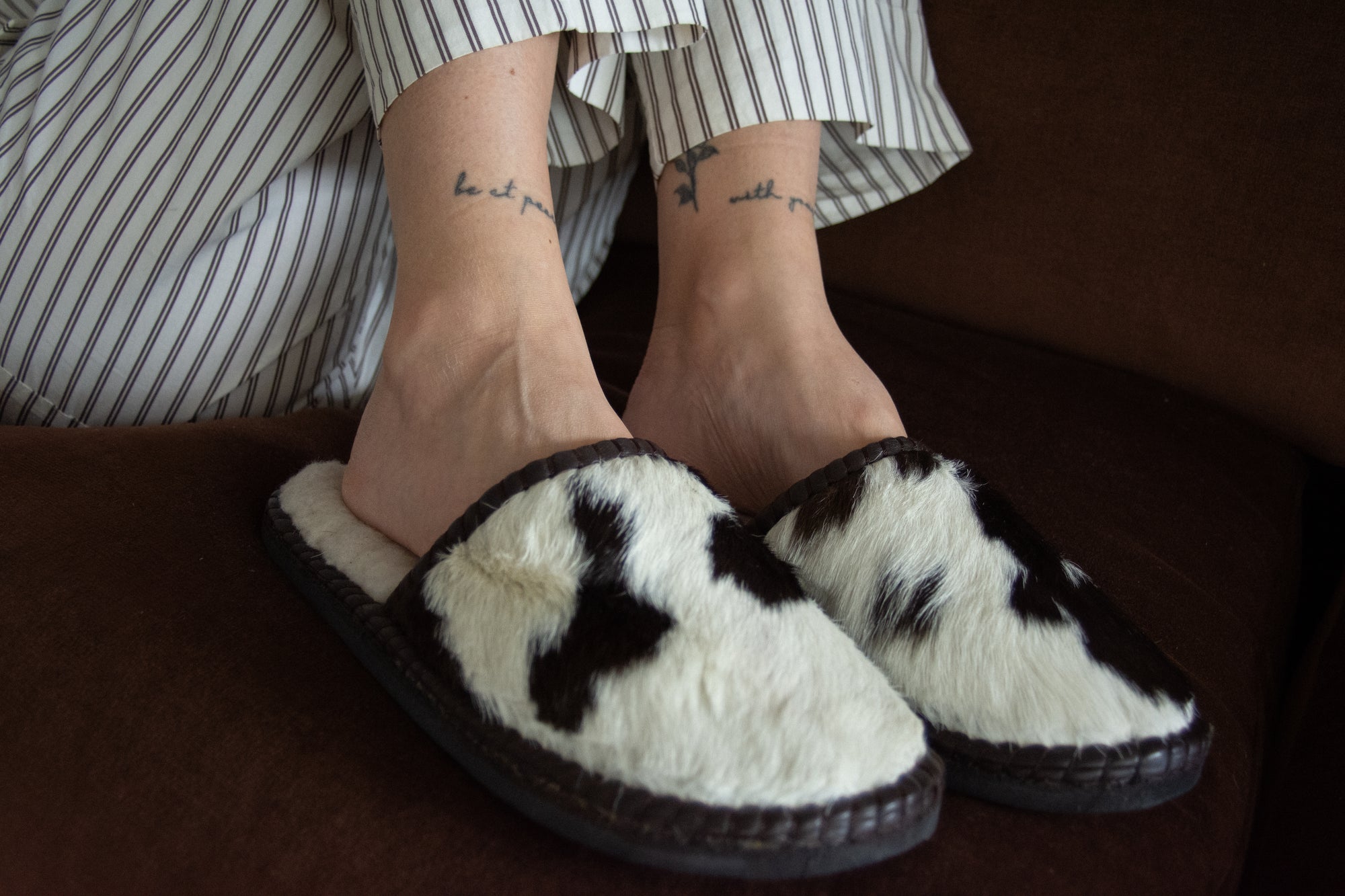 Person wearing white slippers with black patterns on a brown surface