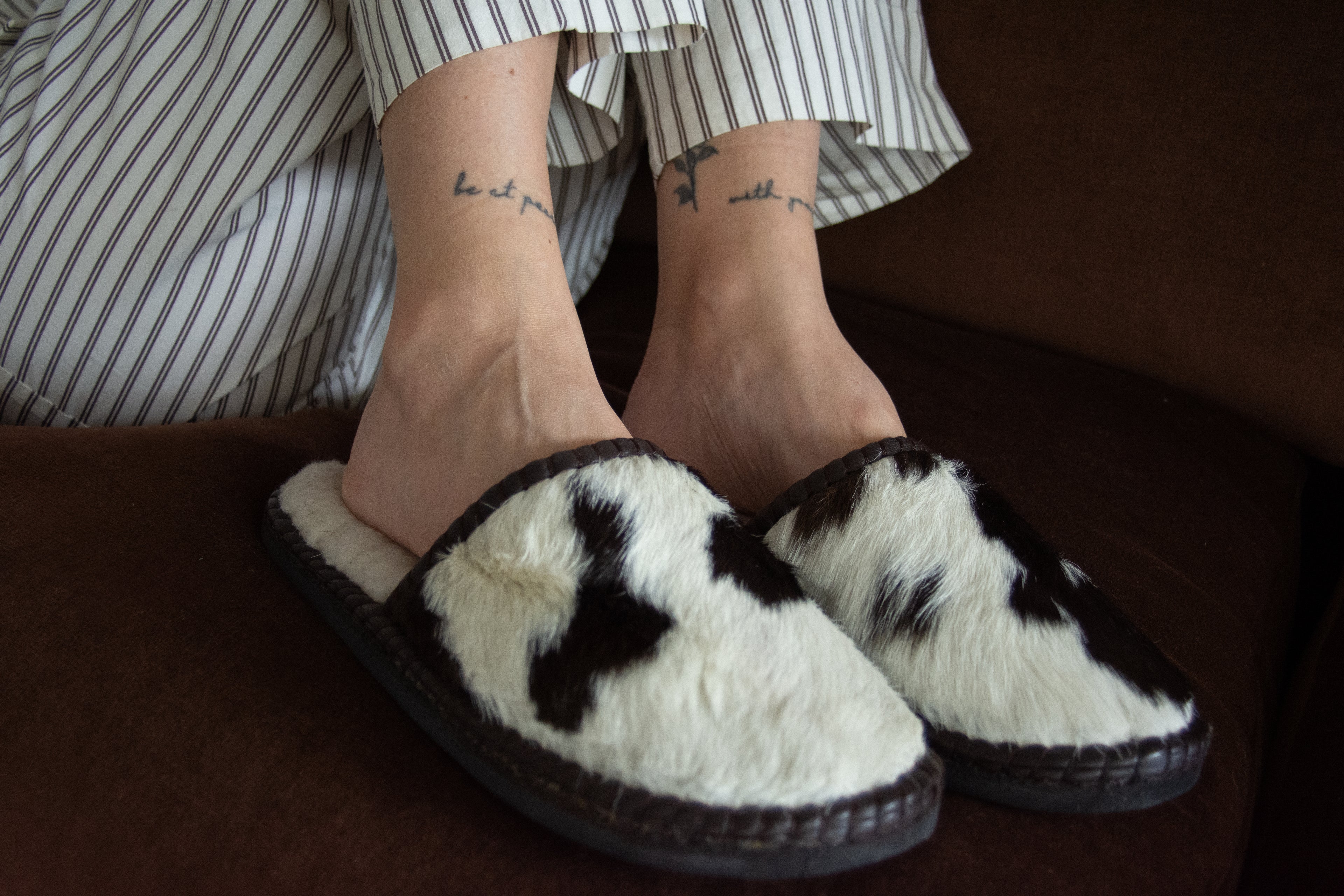 Person wearing white slippers with black patterns on a brown surface